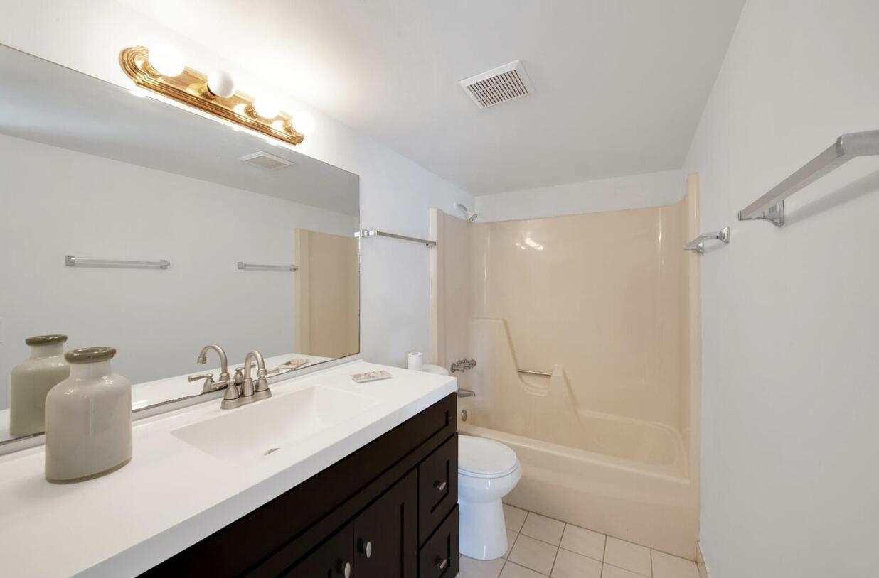A bathroom features a dark vanity with a white countertop, a mirror, and a tub-shower — 3527 La Palmas Court # 1, FL 33463, FL
