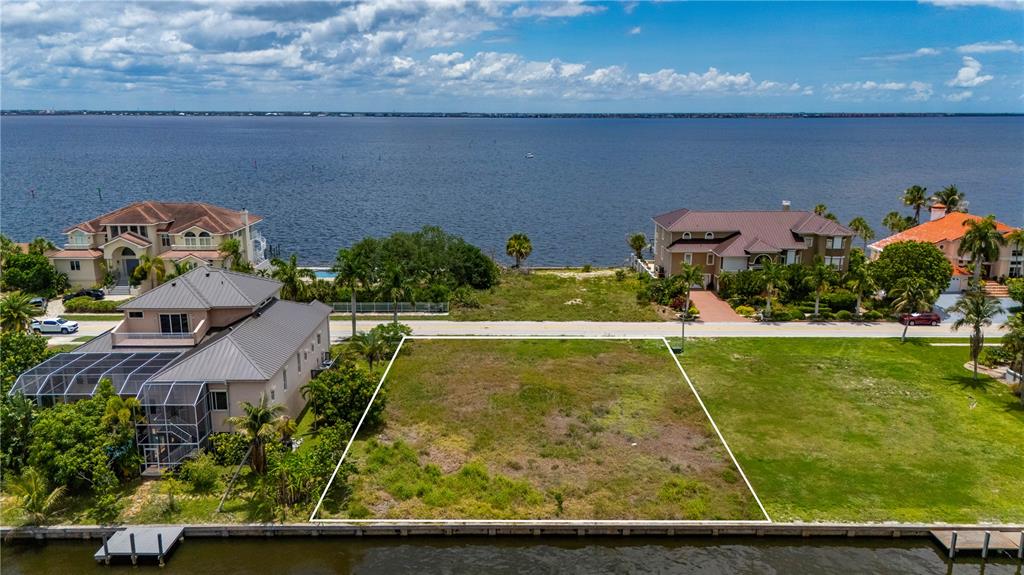 An aerial view shows waterfront homes and a vacant lot along a canal and bay — 238 GEORGE ROAD SE, PORT CHARLOTTE, FL