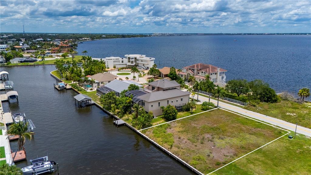 An aerial view shows a vacant waterfront lot situated between two large residential houses — 238 GEORGE ROAD SE, PORT CHARLOTTE, FL