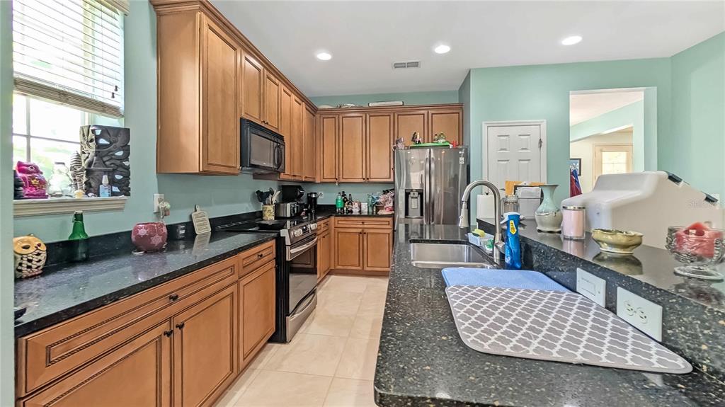 A kitchen features wood cabinets, black countertops, stainless steel appliances, and light-colored tile flooring — 1114 TAPESTRY DRIVE, CELEBRATION, FL