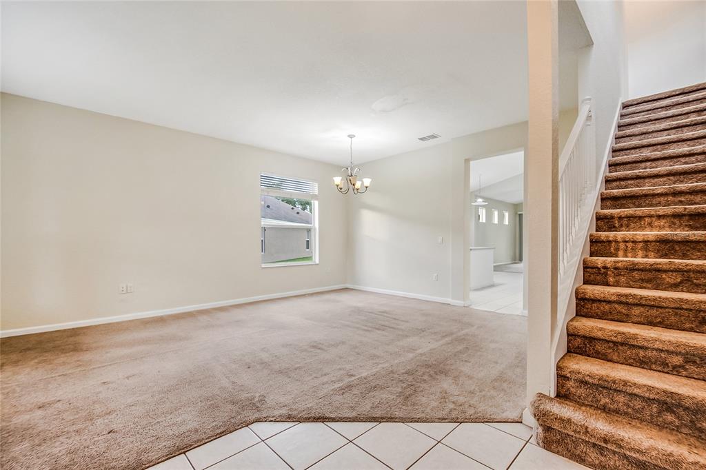 A carpeted living room features a chandelier, a window, and stairs with brown carpeting — 2205 GRANGER AVENUE, KISSIMMEE, FL