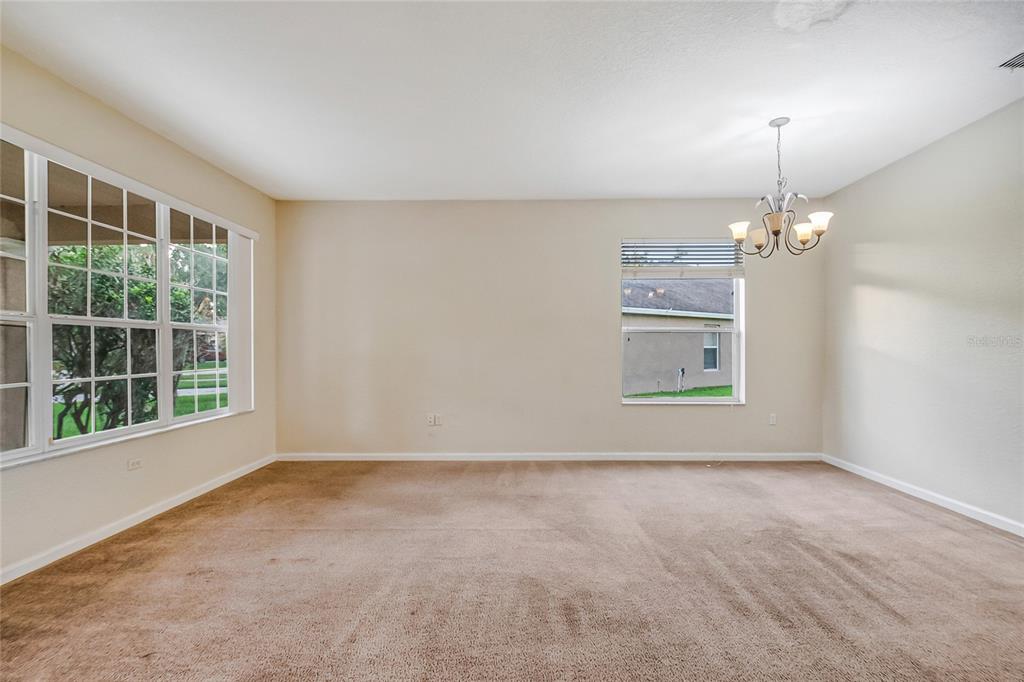 An empty room with beige carpet, light-colored walls, a chandelier, and two windows — 2205 GRANGER AVENUE, KISSIMMEE, FL