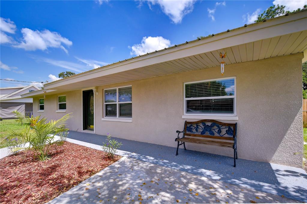 A beige house exterior features a concrete porch, a wooden bench, and a small garden — 3423 PALM ROAD, LAKELAND, FL