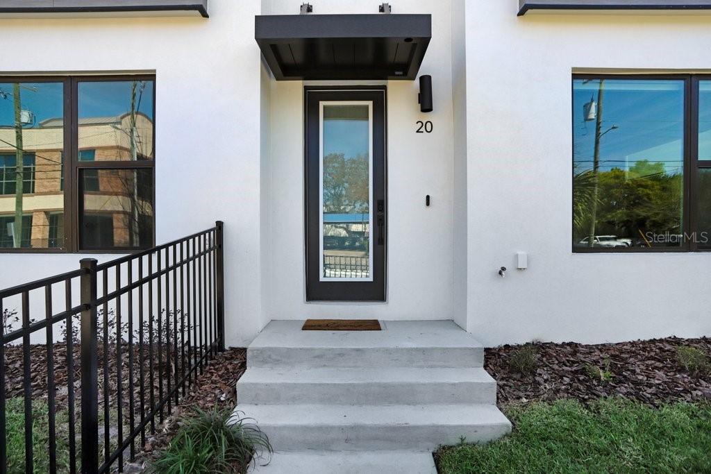 A modern white exterior entrance features a black-framed glass door, concrete steps, and metal railings — 2506 W CLEVELAND STREET UNIT 20, TAMPA, FL