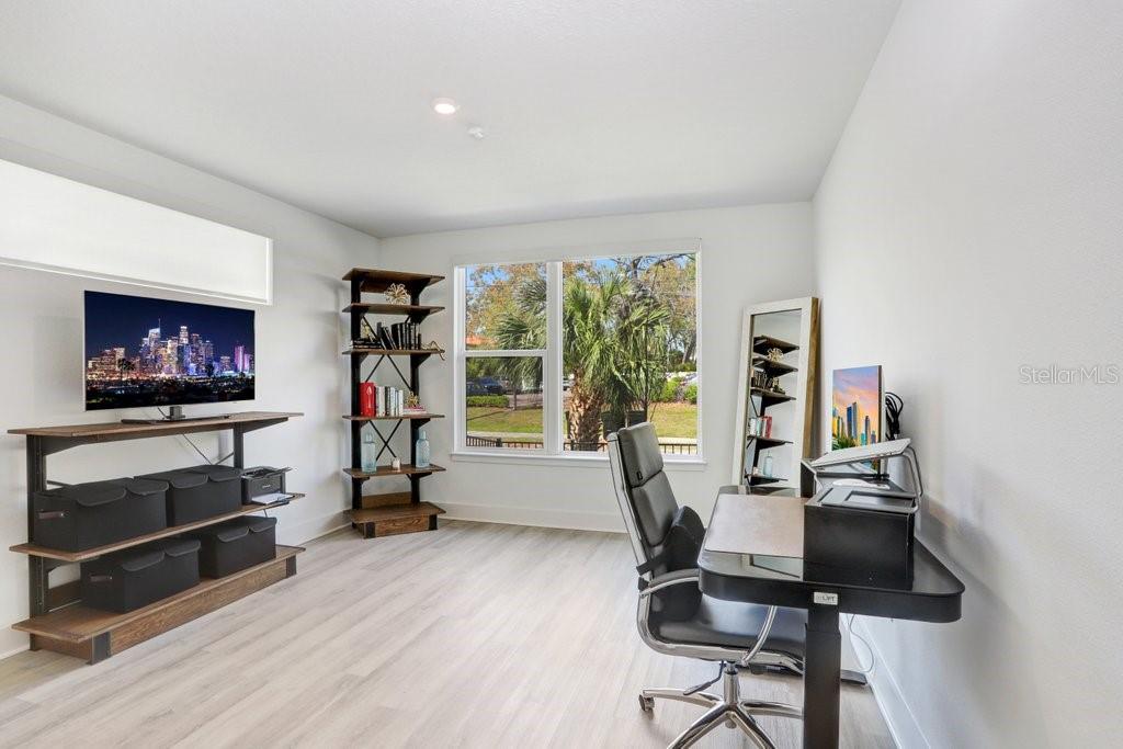 A home office with light wood-look flooring, a desk, a bookshelf, and a wall-mounted television — 2506 W CLEVELAND STREET UNIT 20, TAMPA, FL