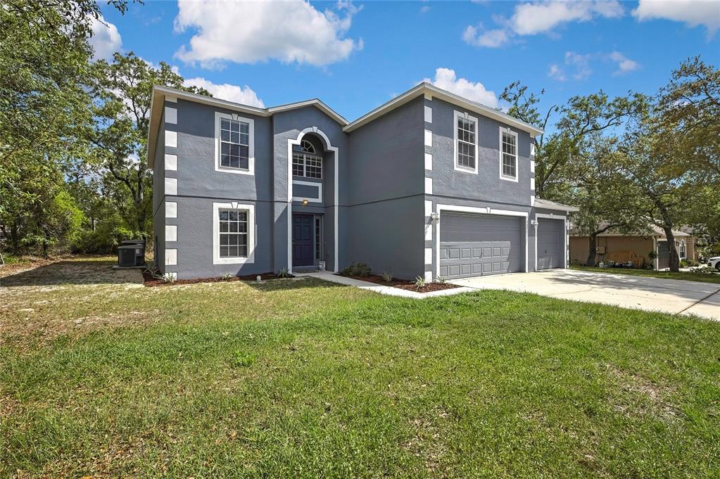 A two-story gray house with white corner accents, a three-car garage, and a front entrance — 11257 PERSIMMON AVENUE, WEEKI WACHEE, FL