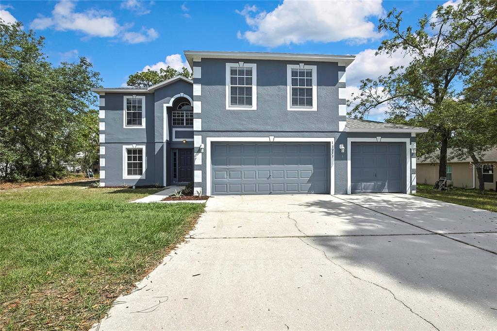 A two-story house with a gray exterior, white corner accents, and a three-car garage — 11257 PERSIMMON AVENUE, WEEKI WACHEE, FL