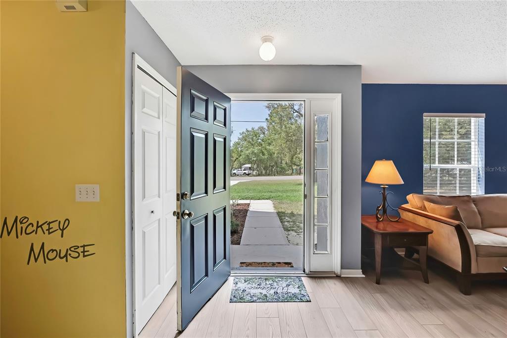 An entryway features a yellow wall with Mickey Mouse lettering, a dark door, and wood flooring — 11257 PERSIMMON AVENUE, WEEKI WACHEE, FL