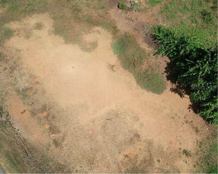 An aerial view of a vacant, grassy lot with a small red marker on the ground — BO. DOMINGUITO, SECTOR LOS COLONOS,, ARECIBO, PR