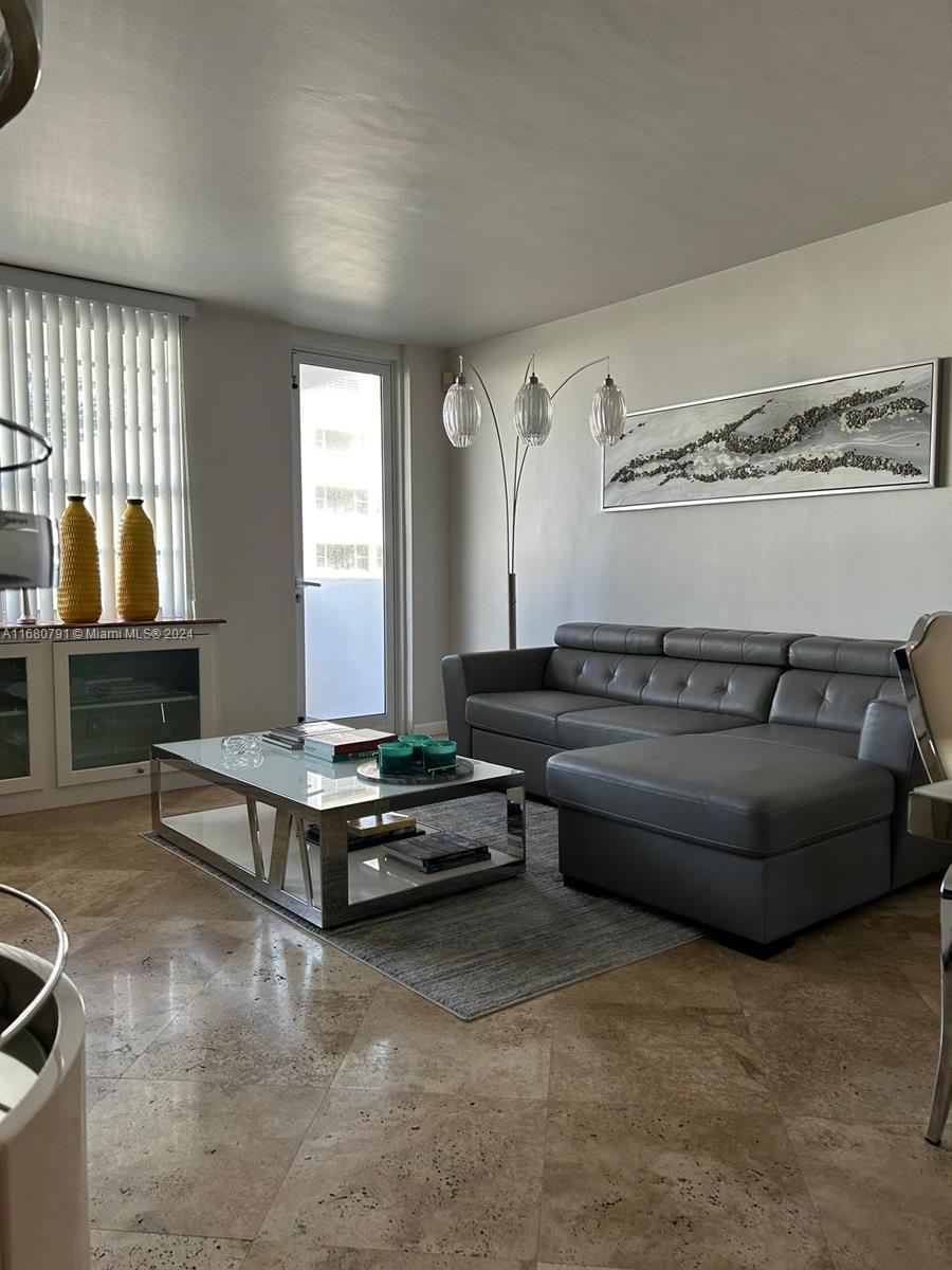 A living room features a grey sectional sofa, glass coffee table, and tile flooring — 100 Lincoln Rd # 608, Miami Beach FL 33139, MIAMI BEACH, FL