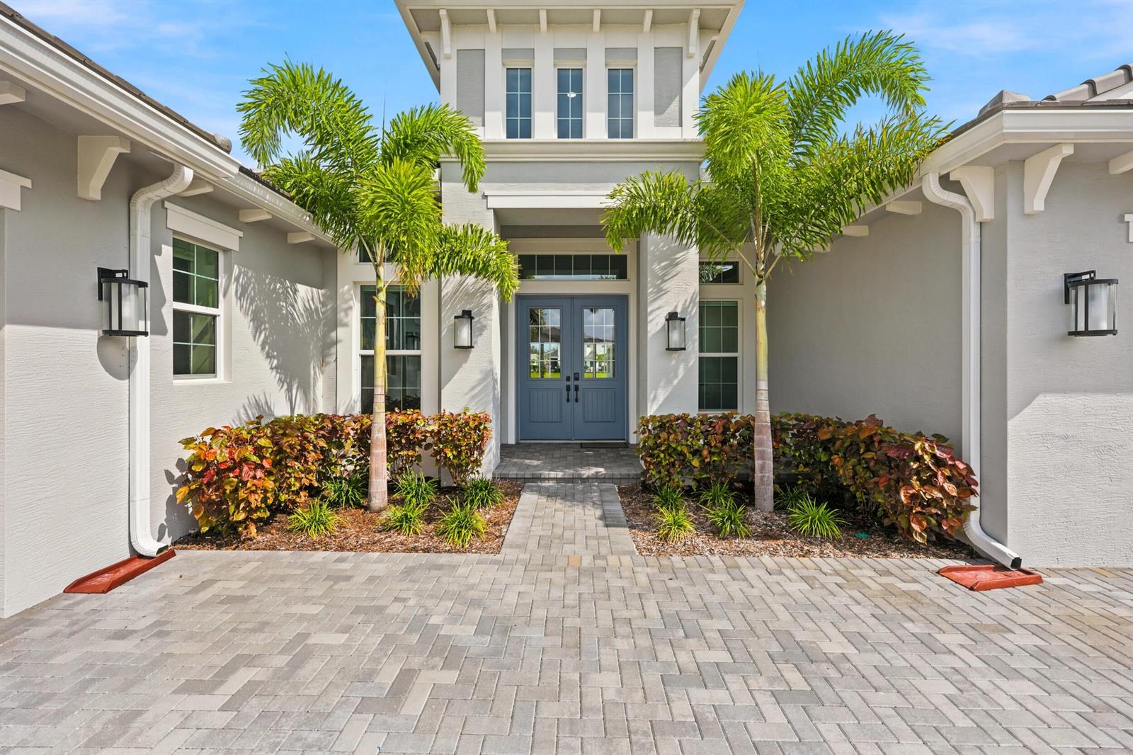 The exterior of a house features a paved walkway leading to blue double front doors — 14831 Wildwood Circle, Westlake FL 33470, WESTLAKE, FL