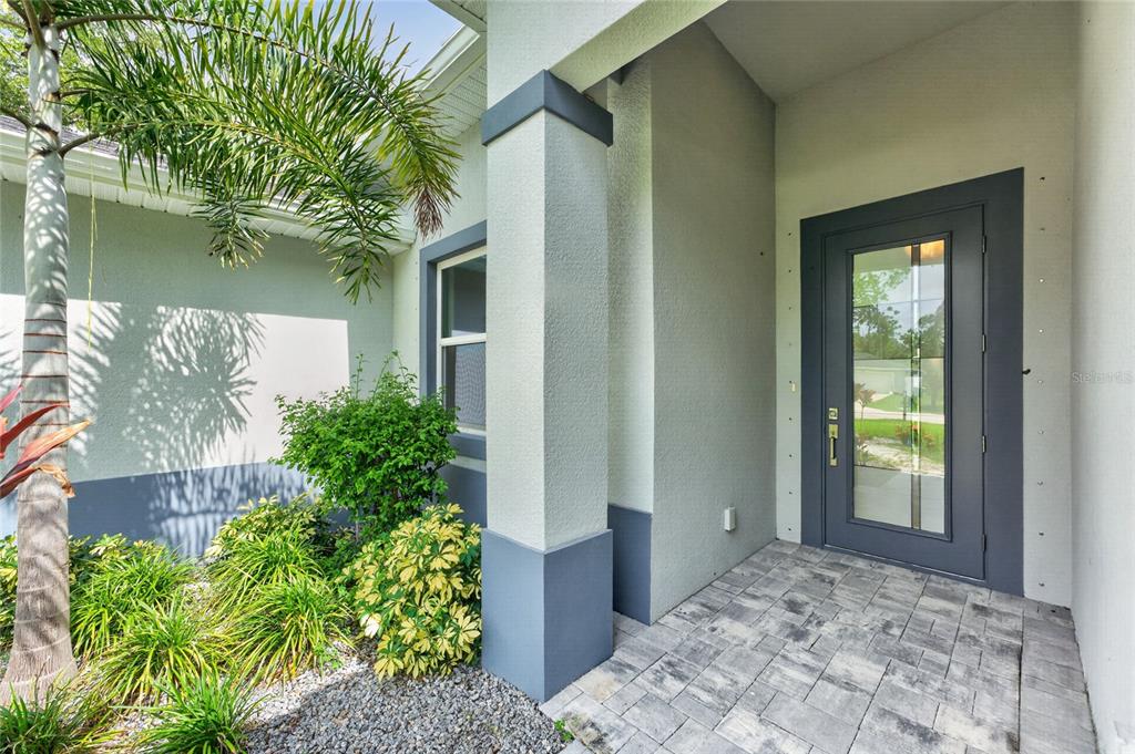 A gray front door with a glass panel sits under a covered entryway with pavers — 14422 CHAMBERLAIN BOULEVARD, PORT CHARLOTTE, FL