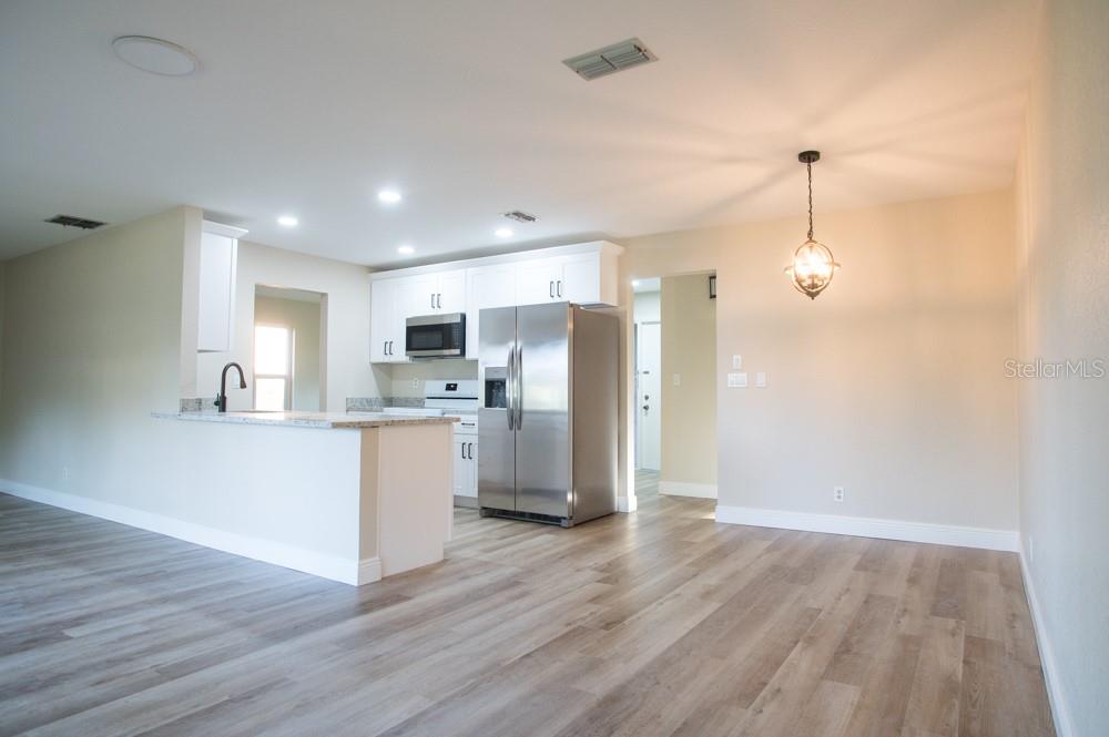 A kitchen with white cabinets and stainless steel appliances opens to a light-floored dining area — 1350 GLENGARRY DRIVE, PALM HARBOR, FL