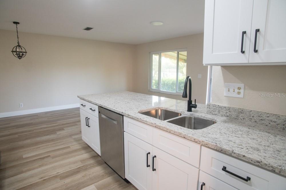 A kitchen features white cabinets, granite countertops, a stainless steel dishwasher, and a double sink — 1350 GLENGARRY DRIVE, PALM HARBOR, FL