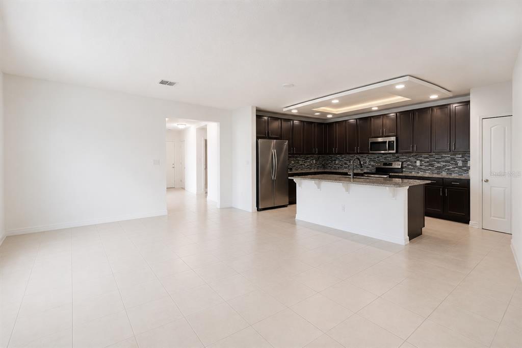 A kitchen with dark cabinets, stainless steel appliances, and an island opens to a room — 507 PINECREST LOOP, DAVENPORT, FL