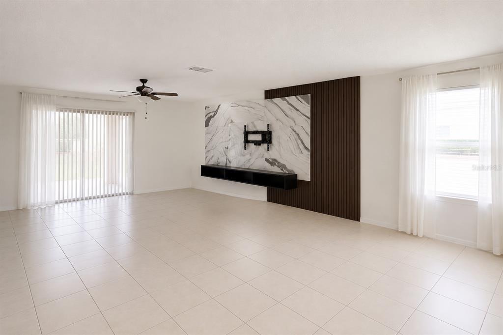 A bright living room features white tile floors, a ceiling fan, and a marble-accented wall — 507 PINECREST LOOP, DAVENPORT, FL