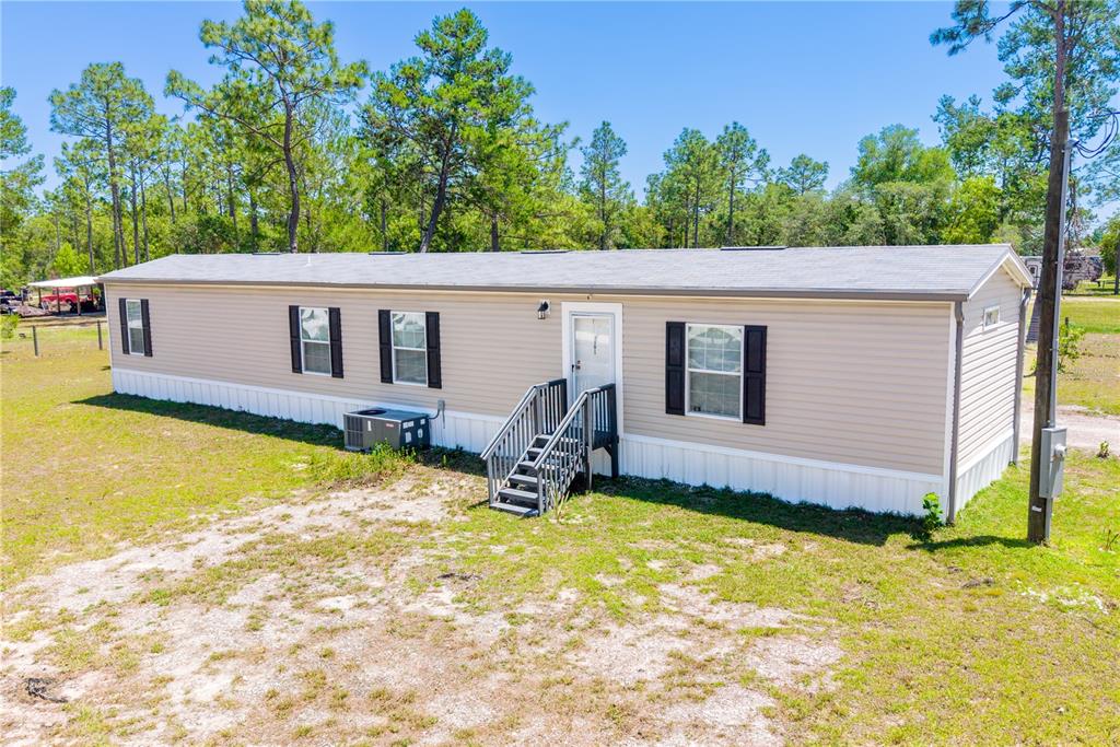 An exterior view of a single-wide manufactured home with tan siding and dark shutters — 191 NE 136TH COURT, WILLISTON, FL