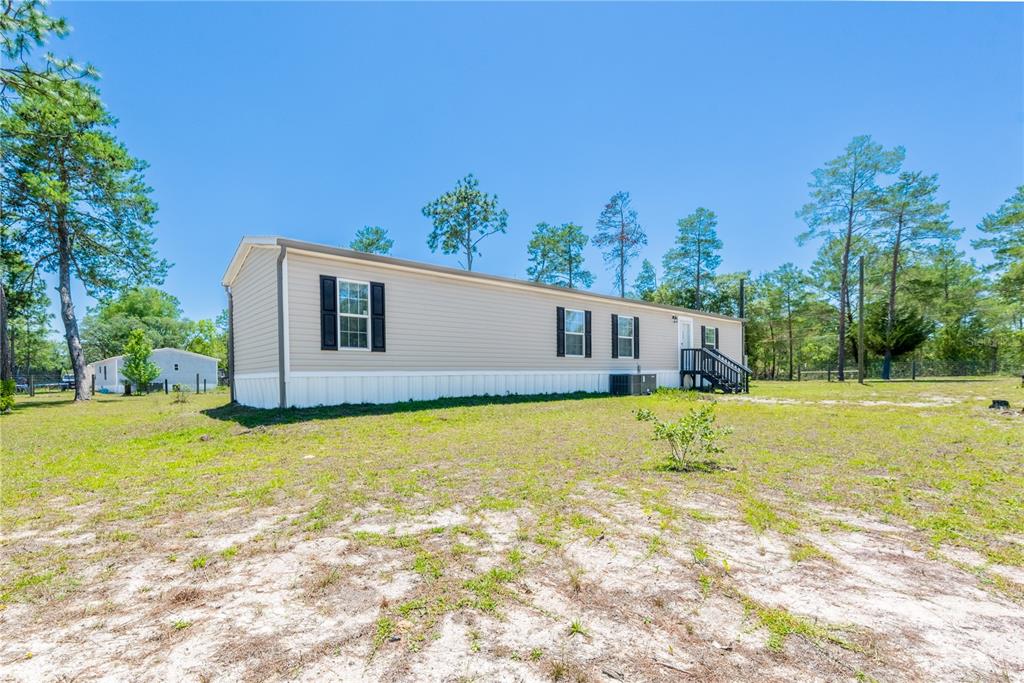A beige manufactured home sits on a large, grassy lot surrounded by pine trees — 191 NE 136TH COURT, WILLISTON, FL