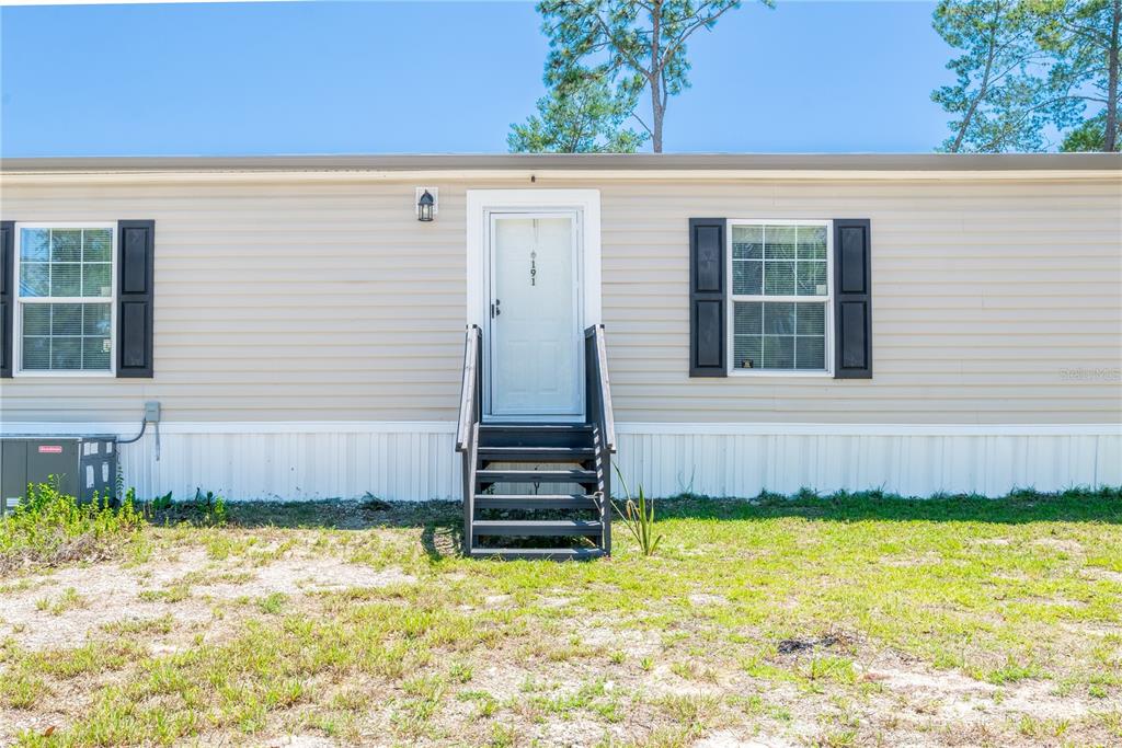 The exterior of a beige manufactured home features a central door, stairs, and two windows — 191 NE 136TH COURT, WILLISTON, FL