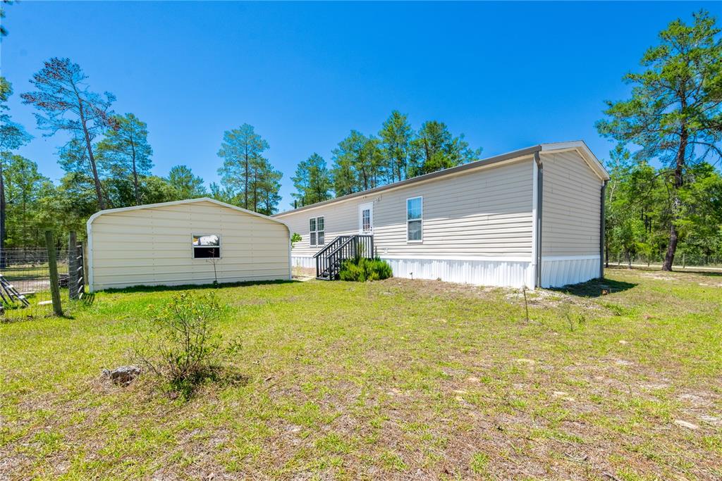 A beige mobile home sits next to a small metal shed on a grassy lot — 191 NE 136TH COURT, WILLISTON, FL