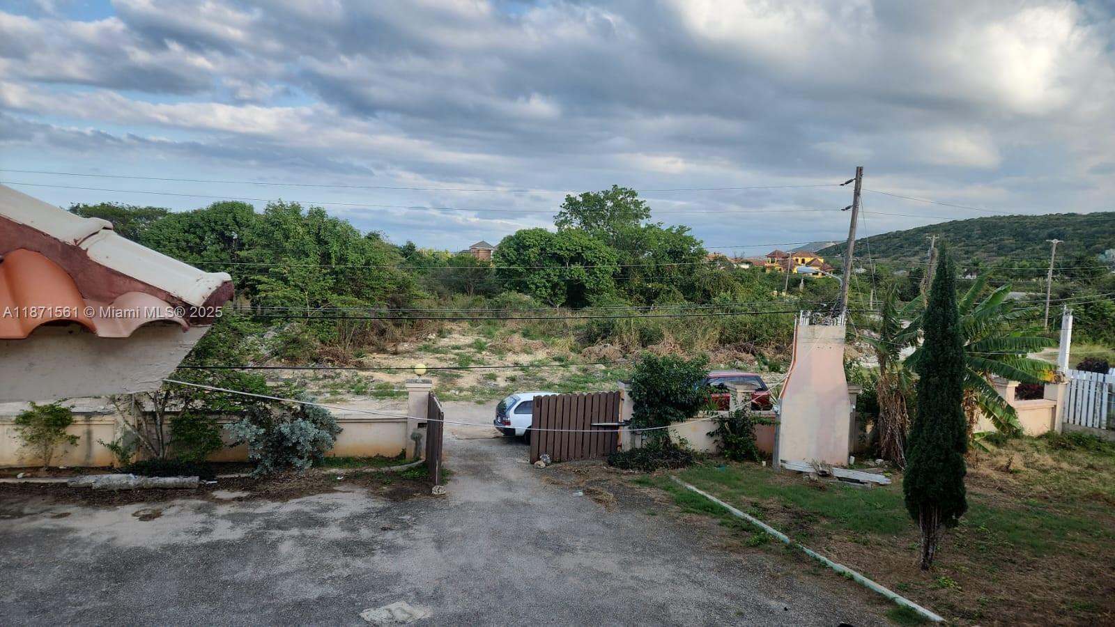 A view from a building overlooking a gated driveway, a vacant lot, and distant hills — 00 WILTSHIRE, TRELAWNY # 00, NA, NA
