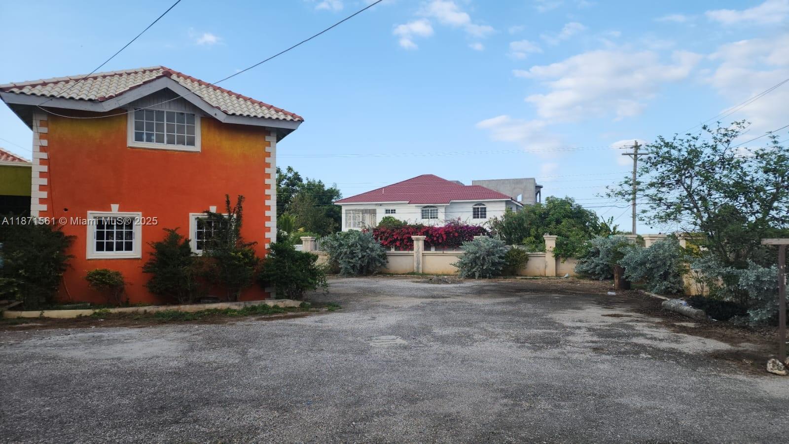 An orange two-story building stands beside a gravel lot facing a white house — 00 WILTSHIRE, TRELAWNY # 00, NA, NA