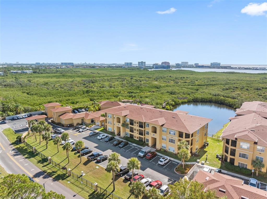 An aerial view shows apartment buildings with tan stucco walls and brown roofs near a pond — 4345 BAYSIDE VILLAGE DRIVE UNIT 302, TAMPA, FL