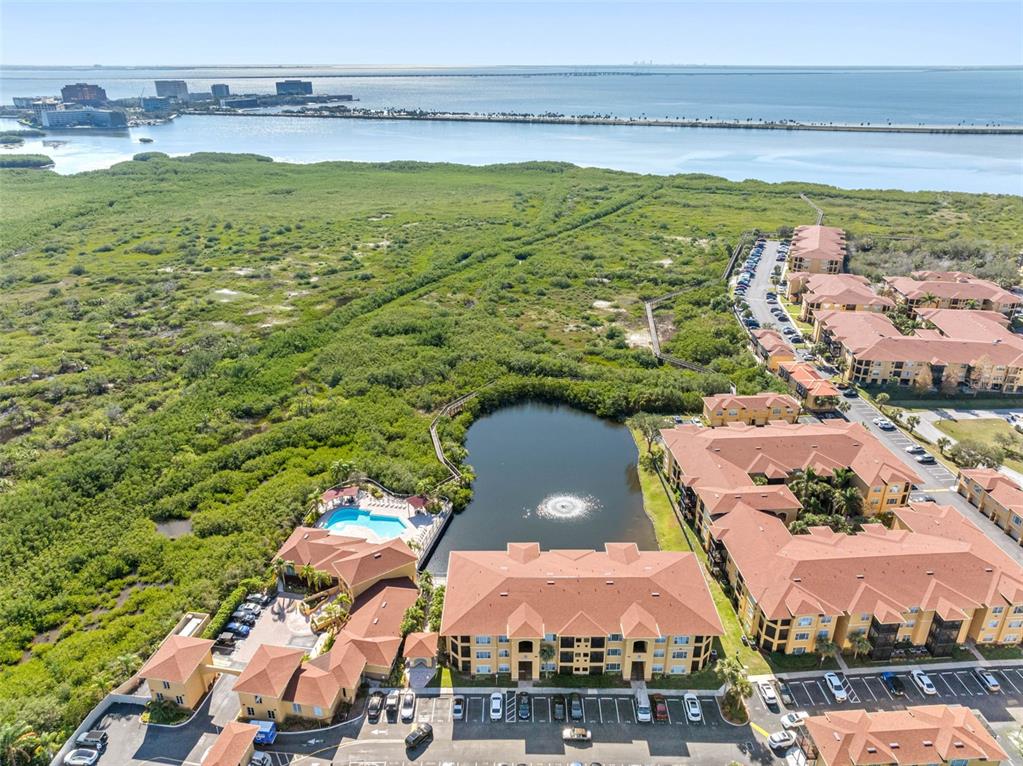 An aerial view shows a multi-story apartment complex with a pool beside a small lake — 4345 BAYSIDE VILLAGE DRIVE UNIT 302, TAMPA, FL