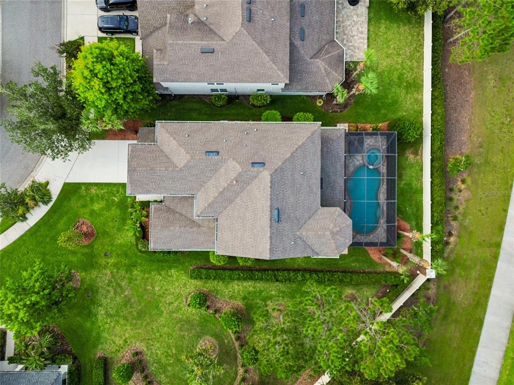 An aerial view shows a house with a shingled roof, pool enclosure, and landscaped yard — 9323 BELLA VITA CIRCLE, LAND O LAKES, FL
