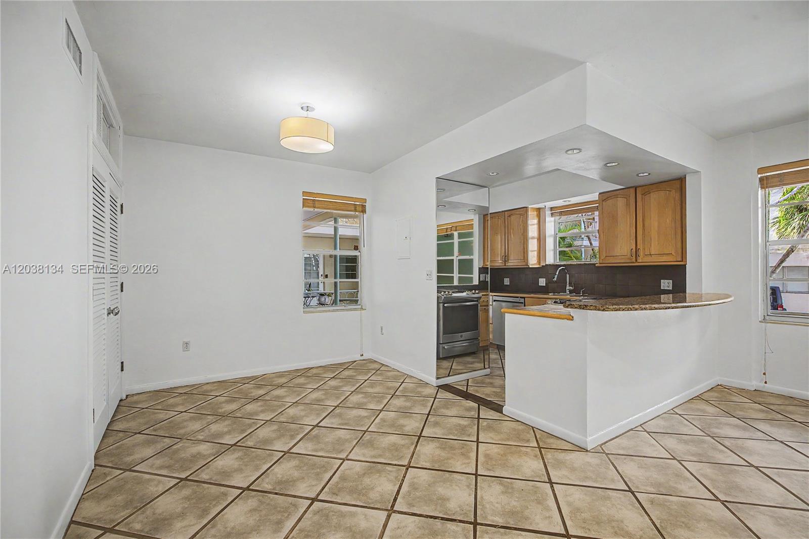 A kitchen with wood cabinets and a granite breakfast bar opens to a tiled dining area — 1751 Washington Ave # 1F, Miami Beach FL 33139, MIAMI BEACH, FL