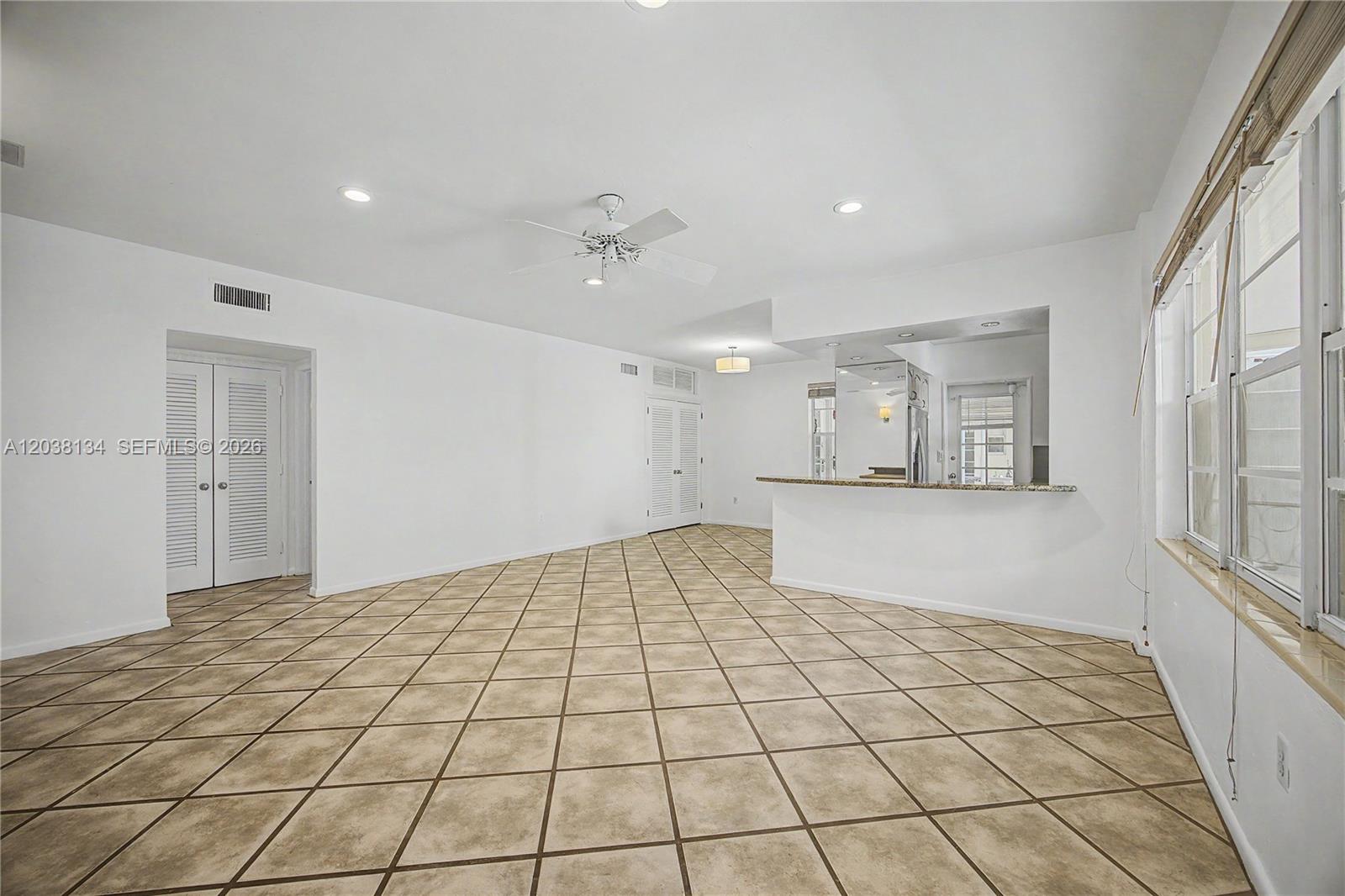 An empty room features diagonal tile flooring, a ceiling fan, and a kitchen pass-through window — 1751 Washington Ave # 1F, Miami Beach FL 33139, MIAMI BEACH, FL