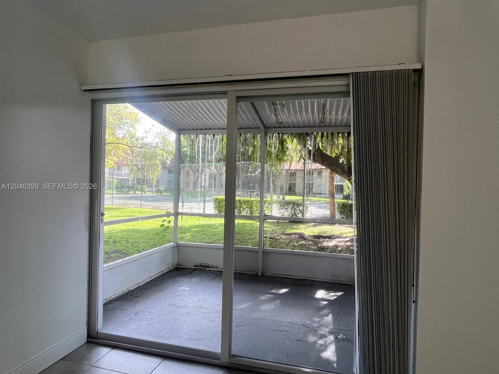 A sliding glass door opens to a screened-in patio overlooking a grassy area and trees — MIAMI, FL