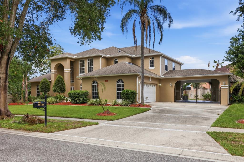 A two-story tan stucco house with a palm tree, driveway, and gated side carport — 10125 FOXHURST COURT, ORLANDO, FL
