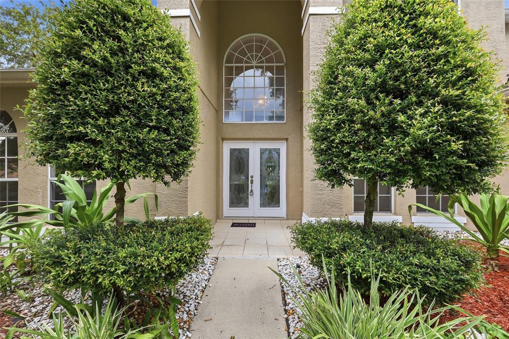 The front entrance of a house features double glass doors, a large arched window, and landscaping — 10125 FOXHURST COURT, ORLANDO, FL