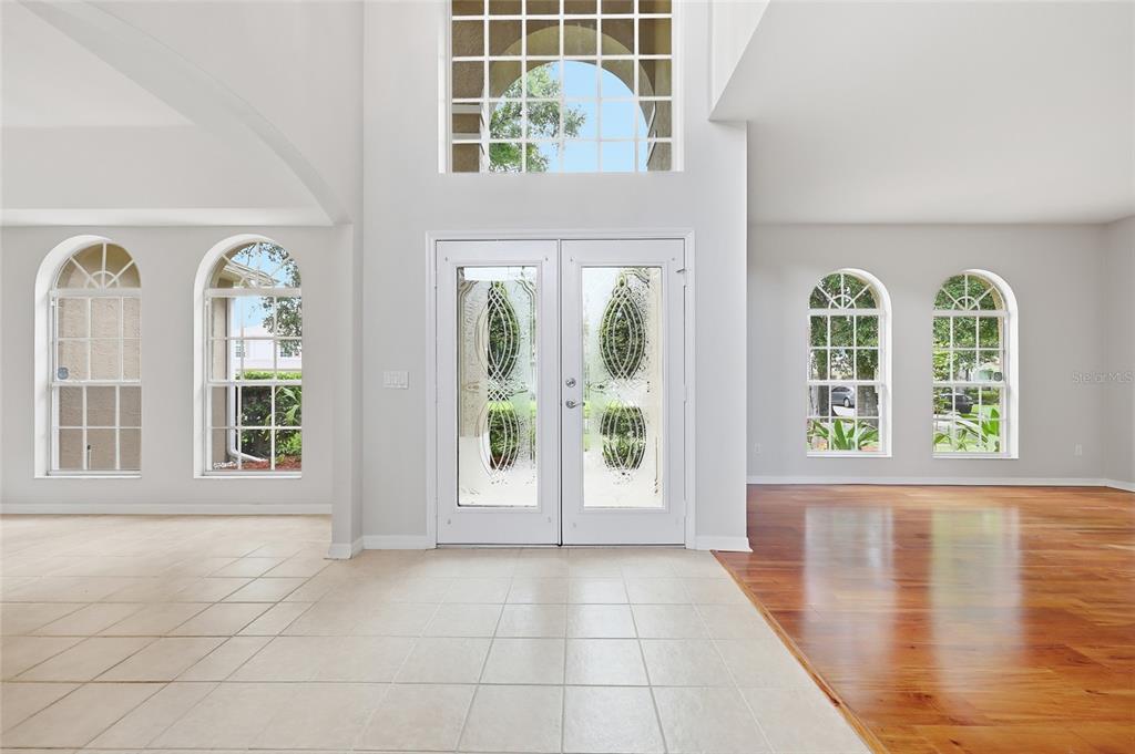 A bright foyer features double glass doors, arched windows, tile flooring, and hardwood floors — 10125 FOXHURST COURT, ORLANDO, FL