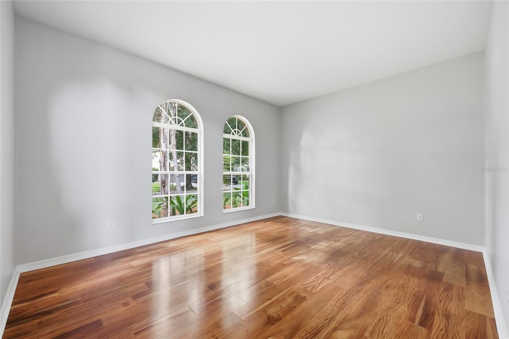 An empty room with light gray walls, hardwood flooring, and two arched windows — 10125 FOXHURST COURT, ORLANDO, FL