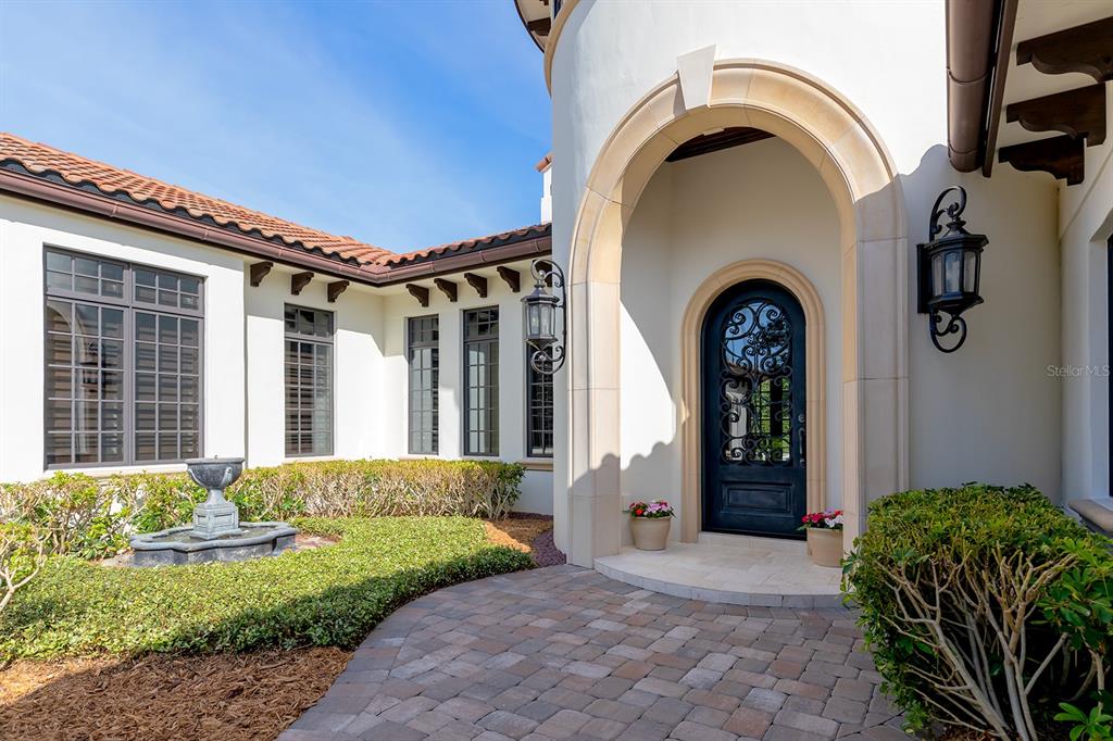 The exterior of a home features a stone-paved entryway, a decorative iron door, and landscaping — 9144 ISLEWORTH GARDENS DRIVE, WINDERMERE, FL