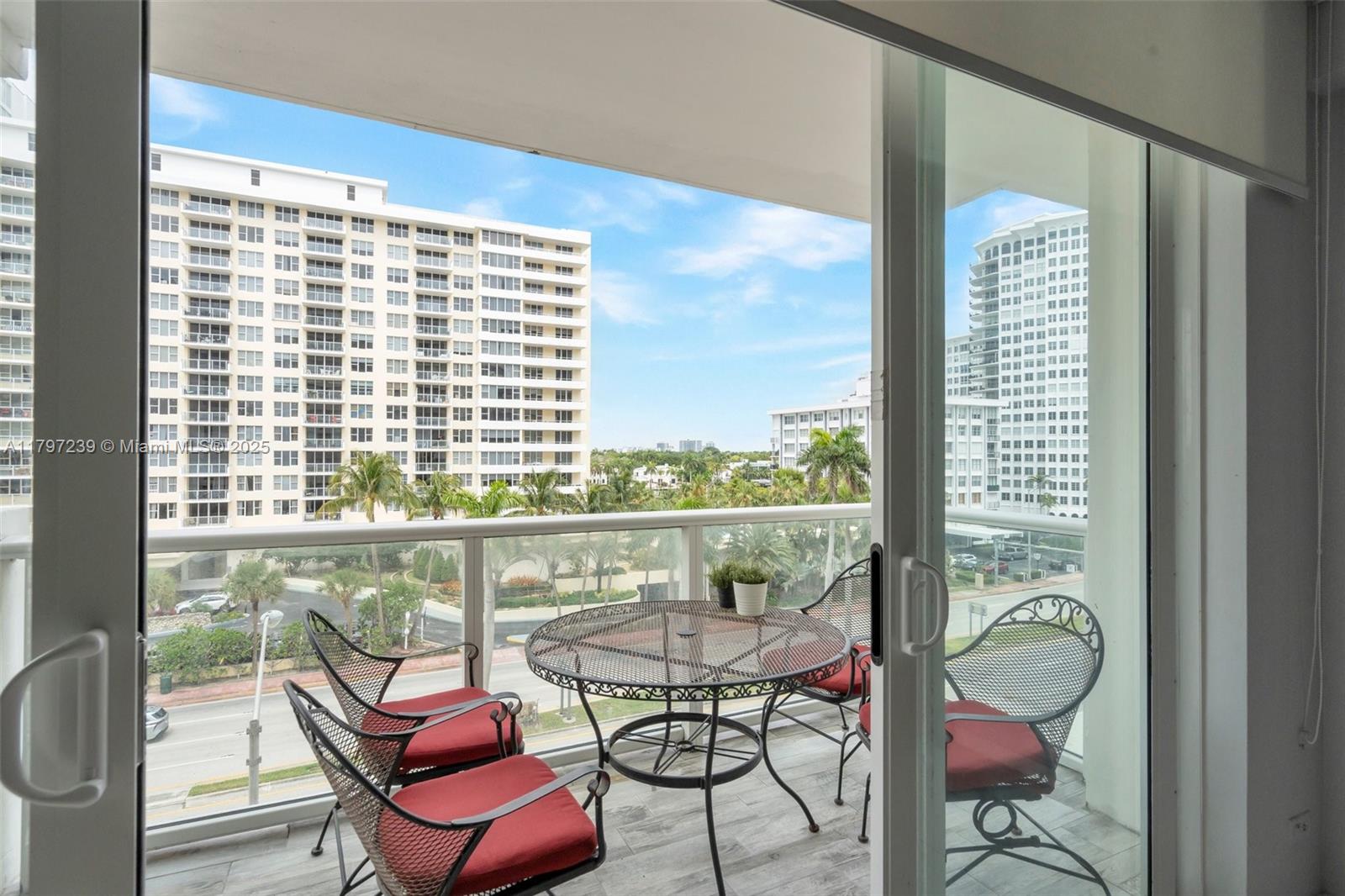 A balcony features a metal table and chairs overlooking a street and neighboring apartment buildings — 5601 Collins Ave # 615, Miami Beach FL 33140, MIAMI BEACH, FL