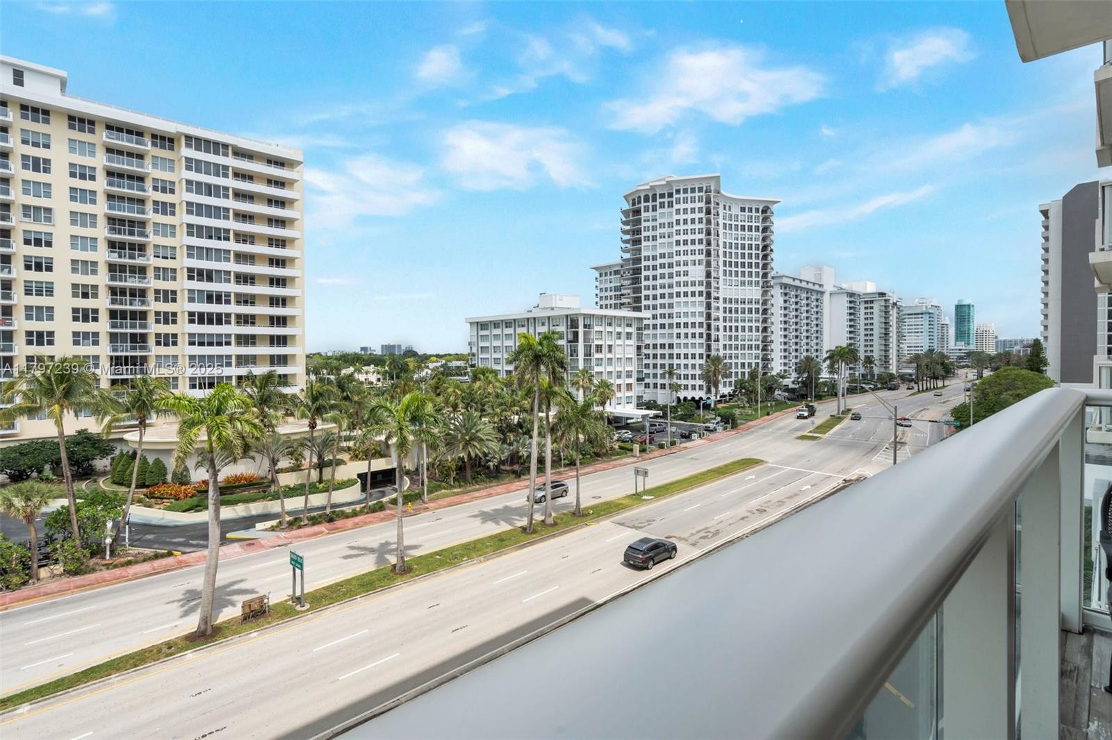 An elevated view from a balcony overlooking a multi-lane road, palm trees, and high-rise buildings — 5601 Collins Ave # 615, Miami Beach FL 33140, MIAMI BEACH, FL