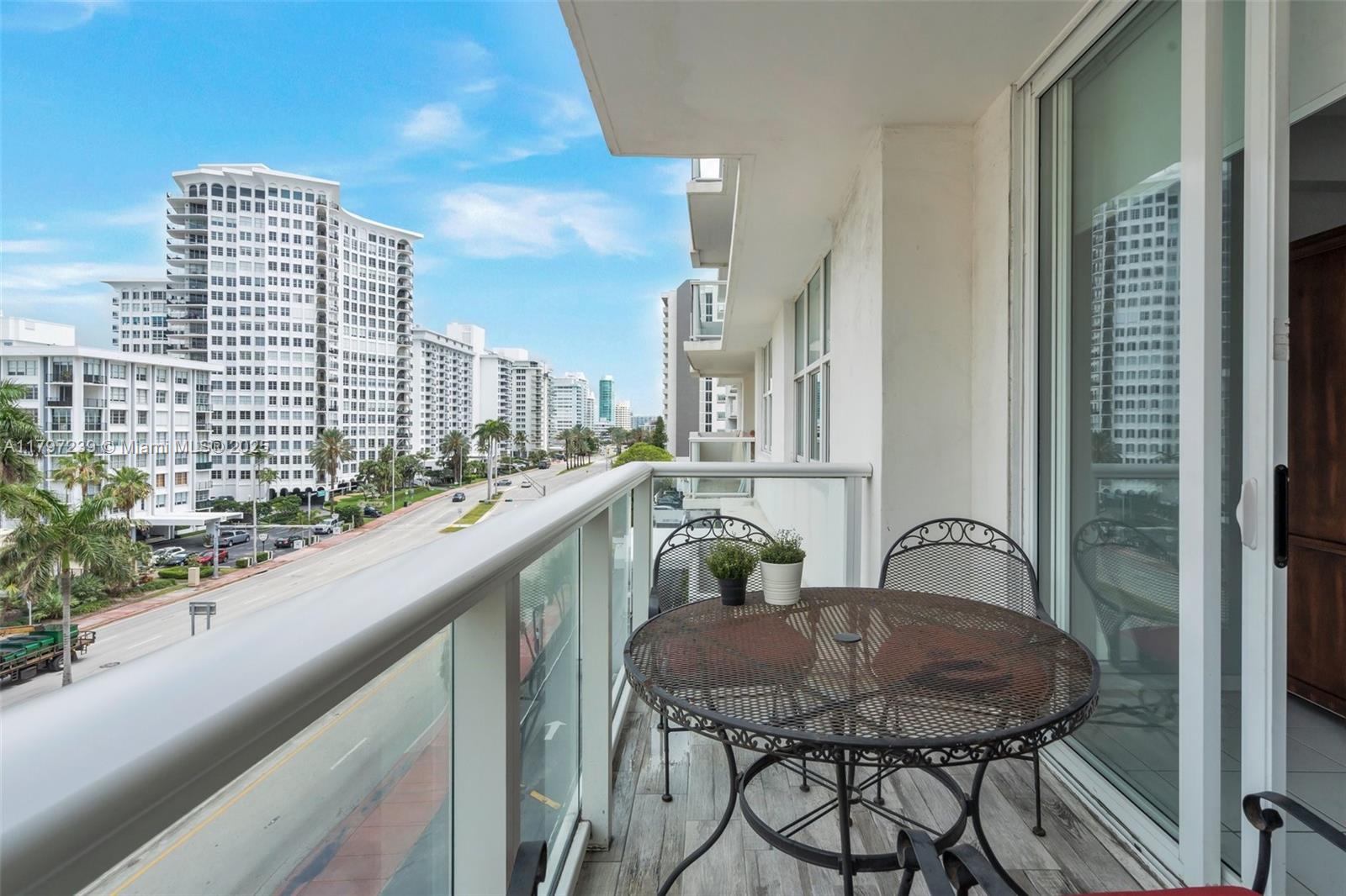A balcony with a metal table and chairs overlooks a city street and tall buildings — 5601 Collins Ave # 615, Miami Beach FL 33140, MIAMI BEACH, FL