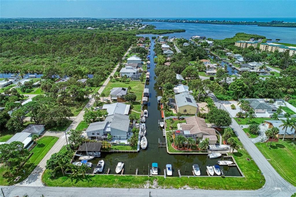An aerial view shows houses lining a canal with docked boats leading to open water — 9130 PINE COVE DRIVE UNIT B82, ENGLEWOOD, FL