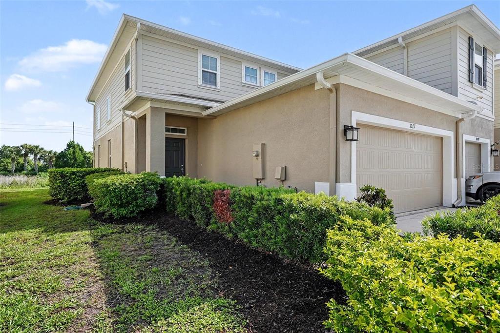 A two-story townhouse exterior features tan siding, a stucco facade, and a single-car garage — 10711 VERAWOOD DRIVE, RIVERVIEW, FL