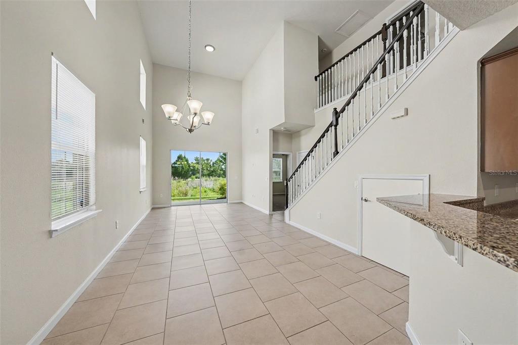 A high-ceilinged dining area features tile flooring, a chandelier, and a staircase with railings — 10711 VERAWOOD DRIVE, RIVERVIEW, FL