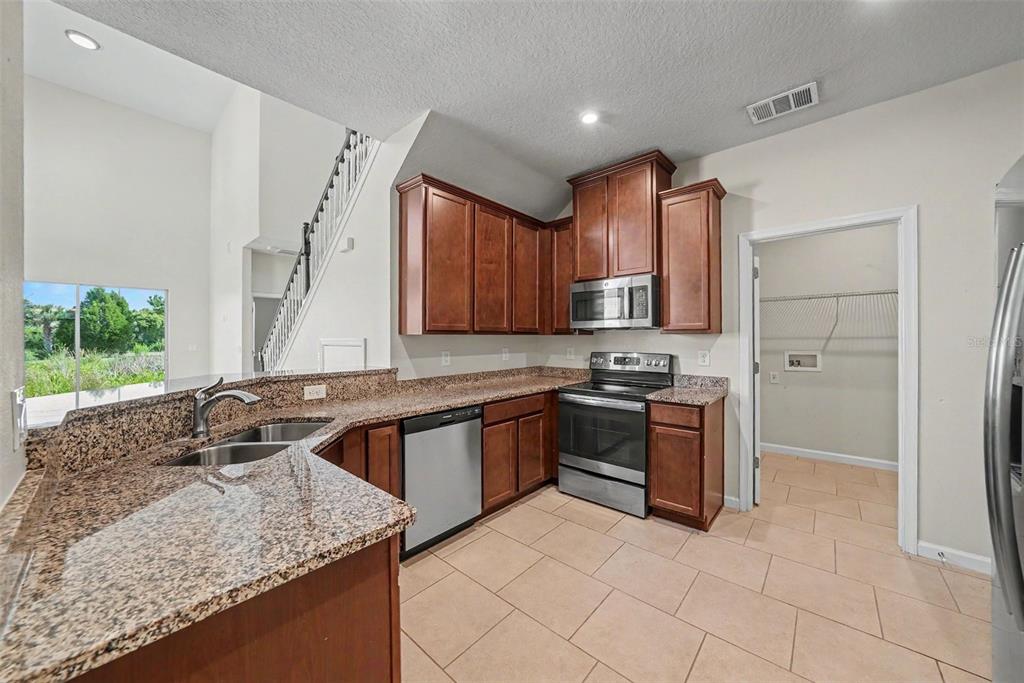 A kitchen with granite countertops, wooden cabinets, stainless steel appliances, and tile flooring — 10711 VERAWOOD DRIVE, RIVERVIEW, FL