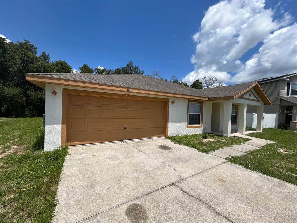 A single-story house with a two-car garage, white stucco walls, and a concrete driveway — 333 GARDENIA COURT, POINCIANA, FL