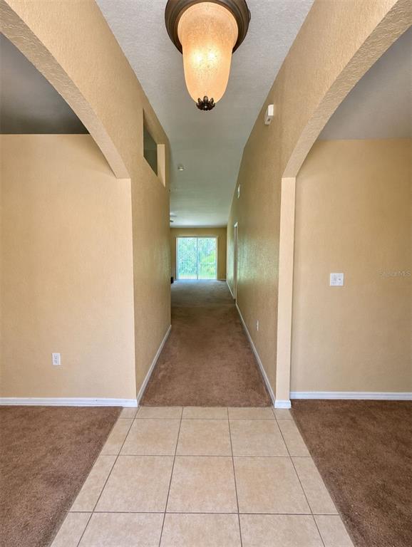 A tiled entryway leads into a carpeted hallway with an arched opening and overhead lighting — 333 GARDENIA COURT, POINCIANA, FL
