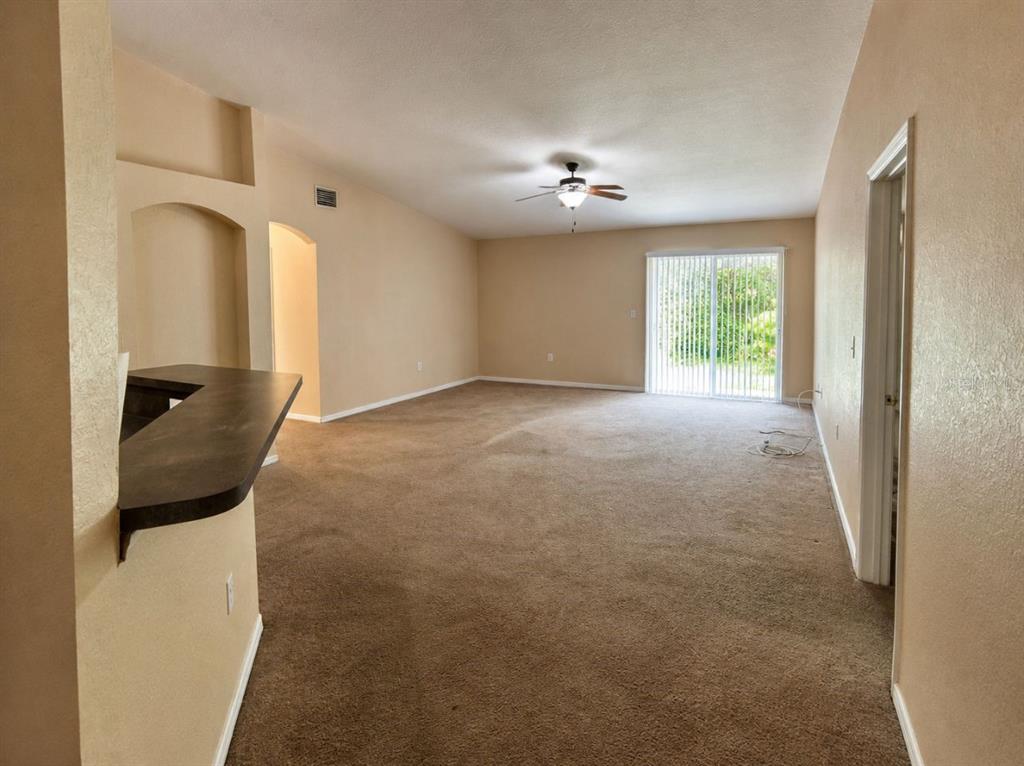 An empty living room features beige carpet, tan walls, a ceiling fan, and sliding glass doors — 333 GARDENIA COURT, POINCIANA, FL