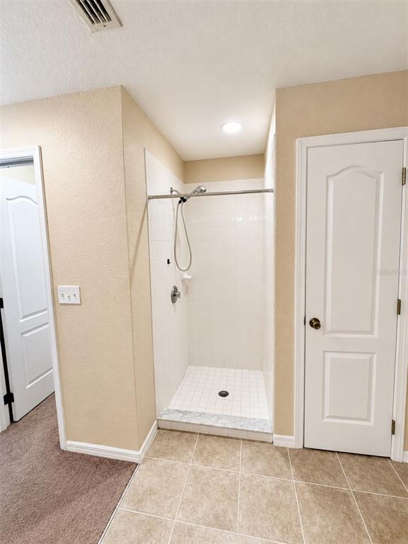 A tiled walk-in shower is situated between two white doors in a neutral-toned room — 333 GARDENIA COURT, POINCIANA, FL