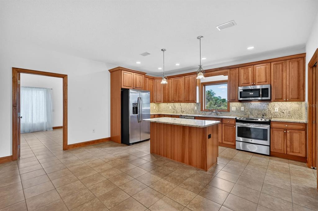 A kitchen with wood cabinets, granite countertops, stainless steel appliances, and a central island — 115 TANGELO TERRACE, CRESCENT CITY, FL