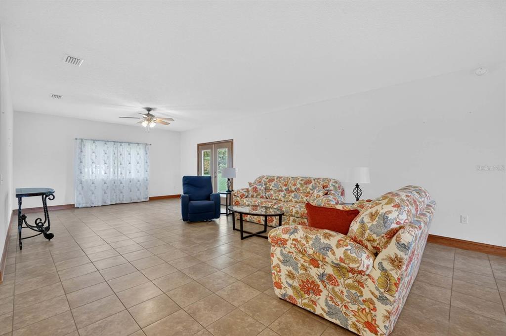 A living room features tile flooring, a floral sofa, a blue recliner, and a ceiling fan — 115 TANGELO TERRACE, CRESCENT CITY, FL